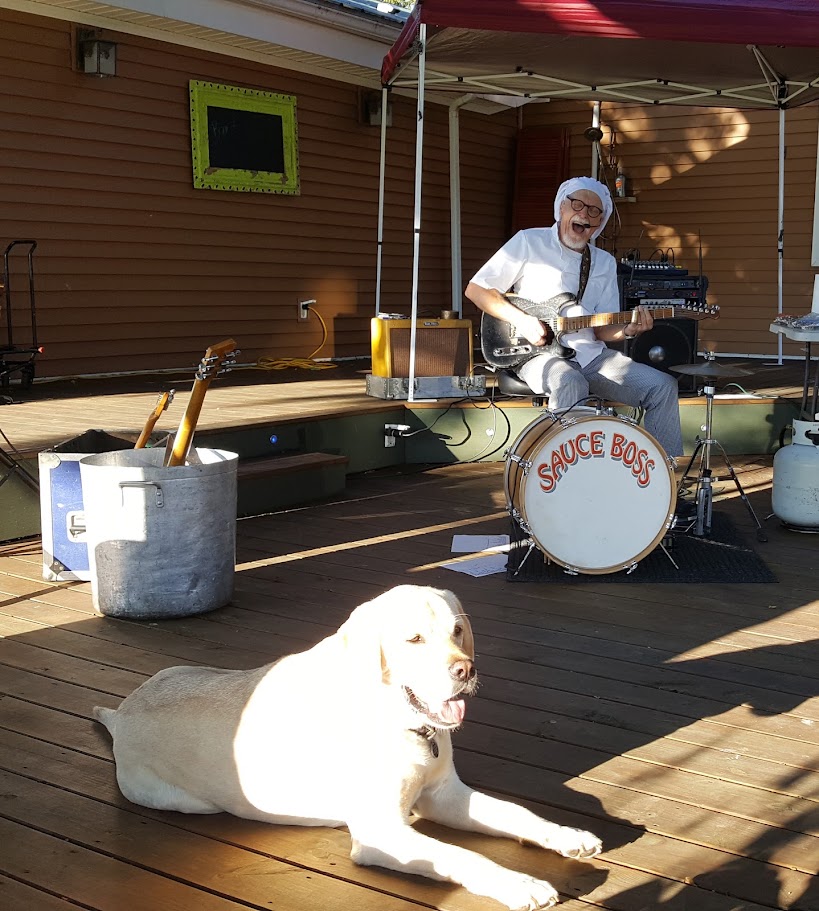 a man sitting playing the guitar on the back deck with Finn the yellow lab laying on the deck