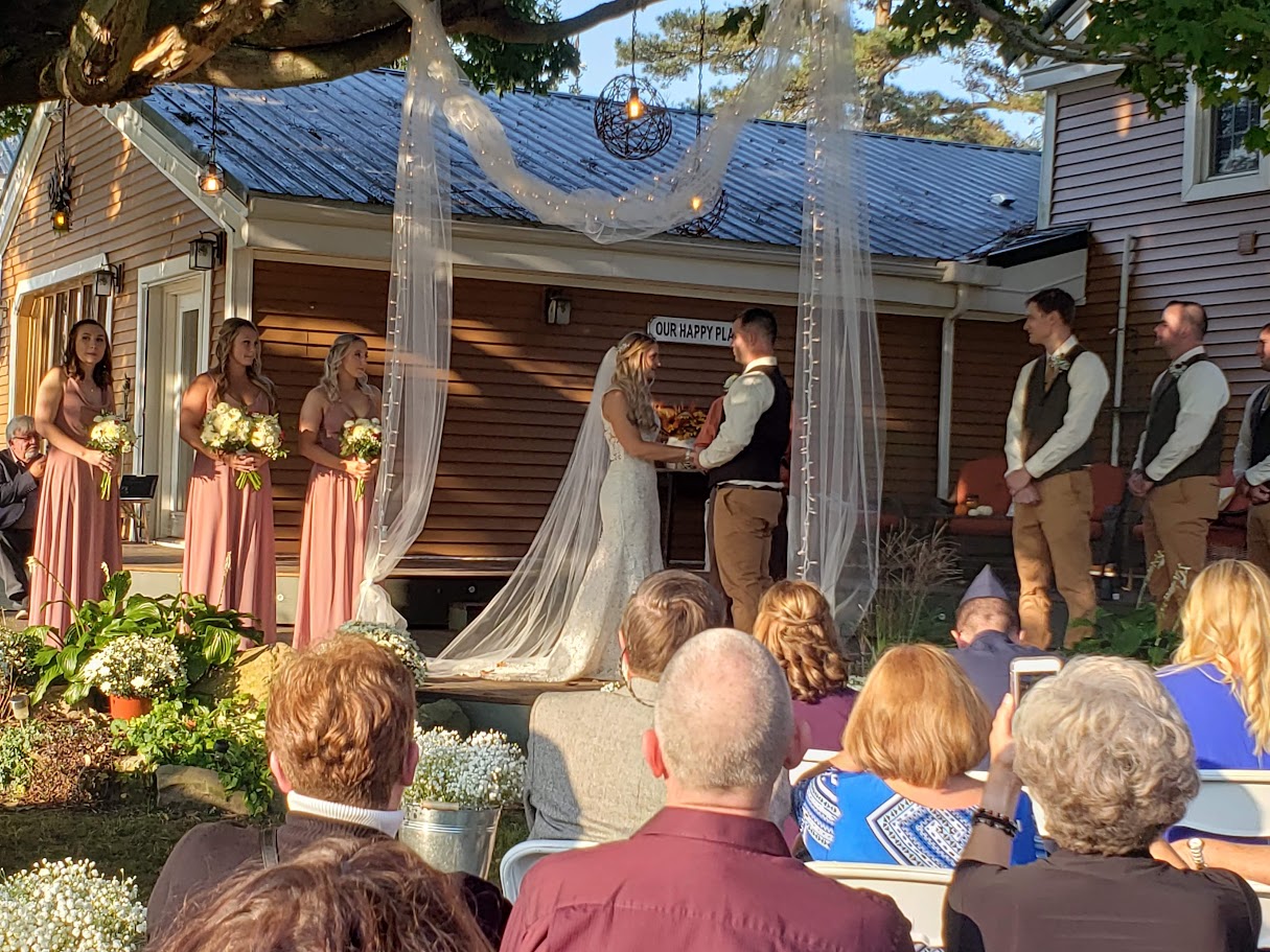 Brand and groom holding hands and exchanging vows with the wedding part standing on both sides and people sitting watching from the audience