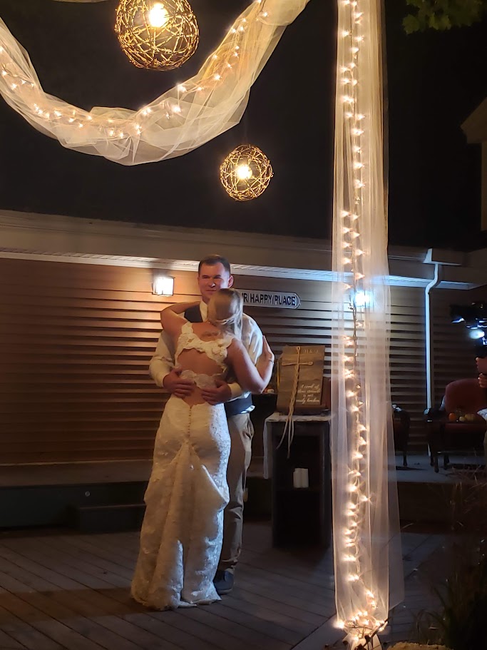 Bride and groom sharing a dance at night time on the back deck with white chiffon and lights in the foreground