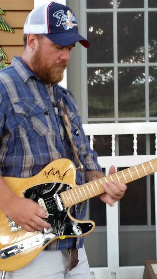 close up of a younger man playing a tan and black electric guitar