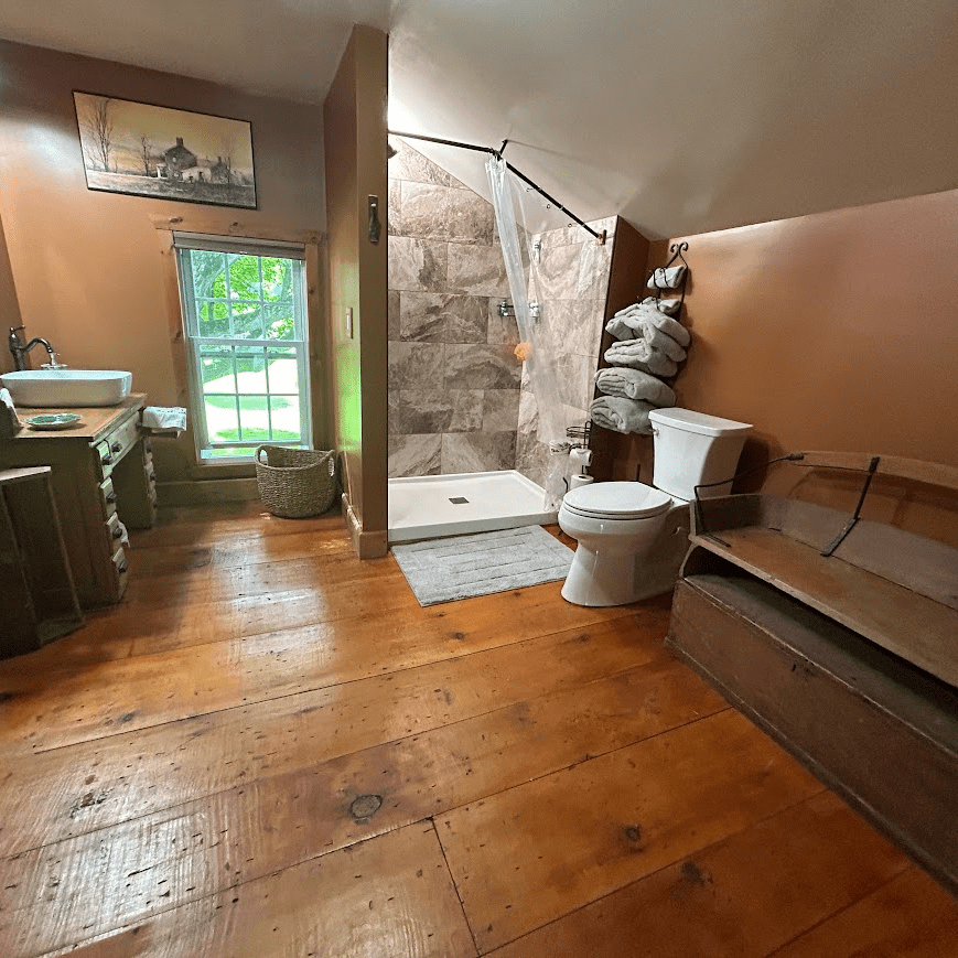 View of the bathroom towards the step in stone shower, towels next to it and a toilet and a sink to the left