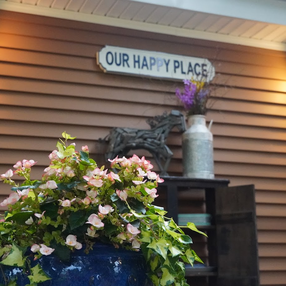 view of the back patio with a pink flower in a blue flower pot against the sign that says "Our Happy place"