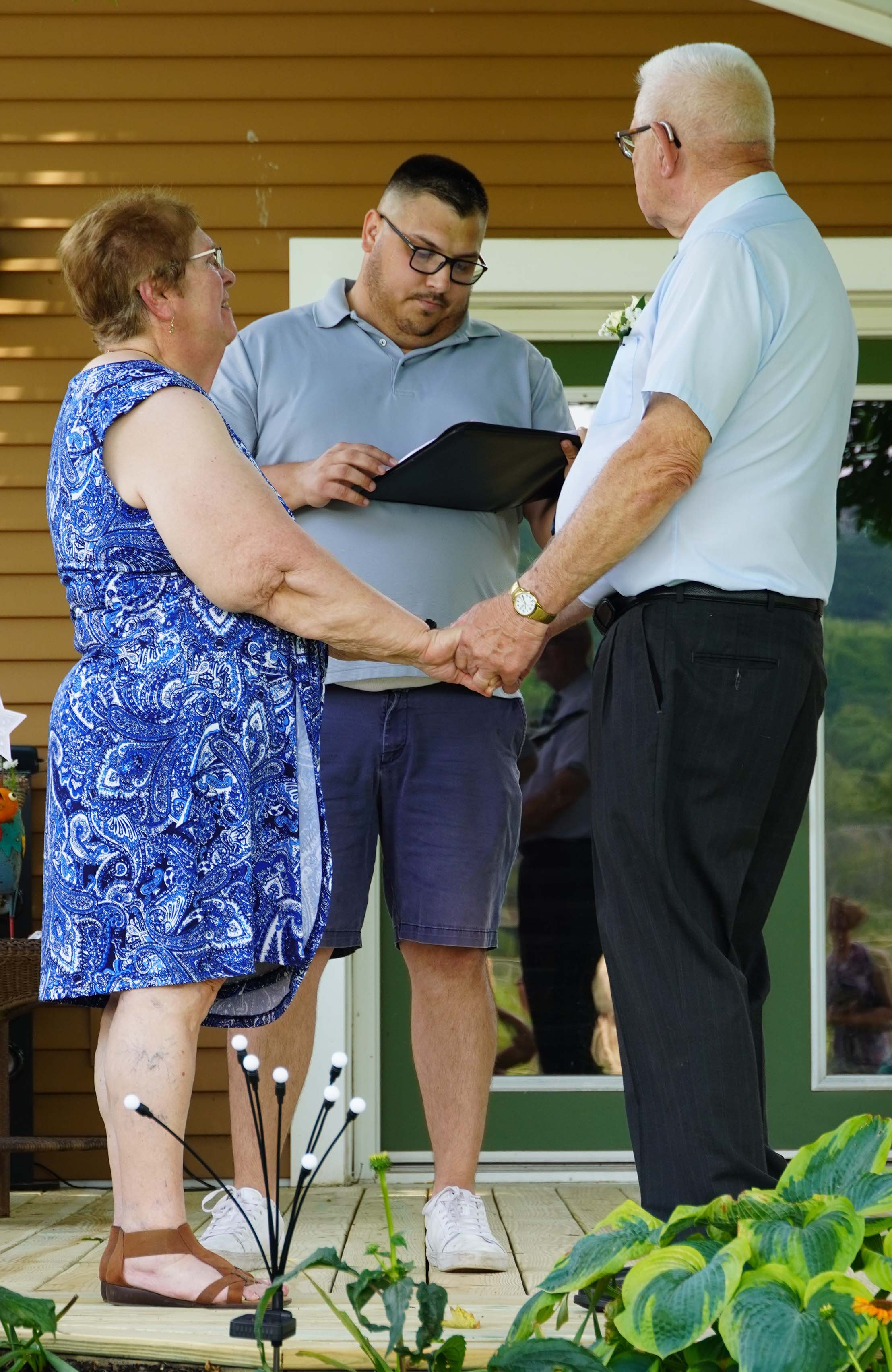 An older couple on the back deck holding hands renewing their vows with a minister behind them