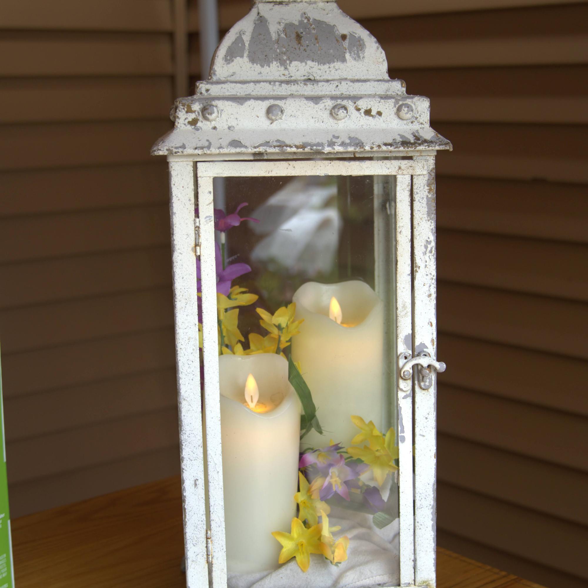close up of a see through white light with two candles inside with yellow and purple flowers
