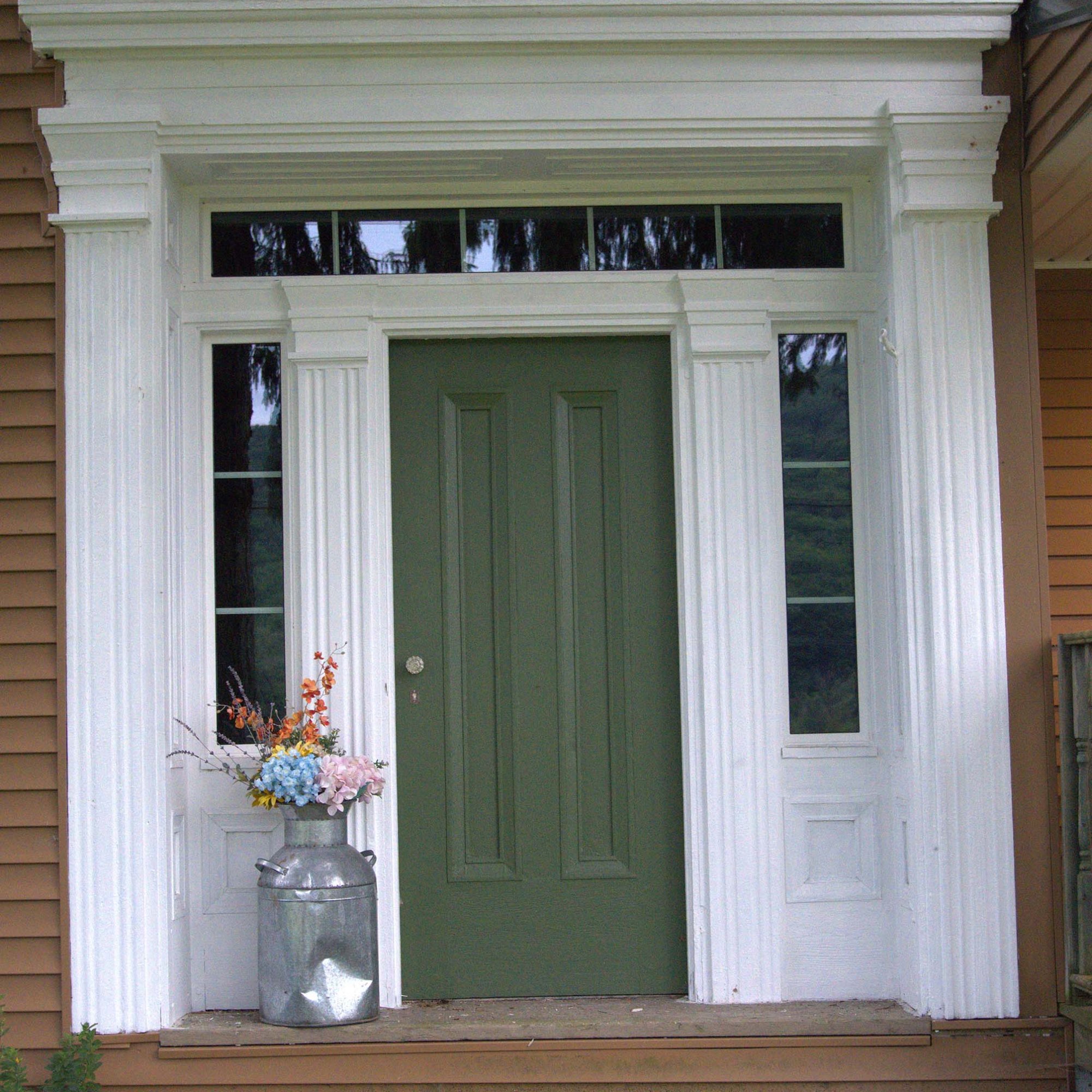 dark green front door with square windows framing it and white trim against the tan house