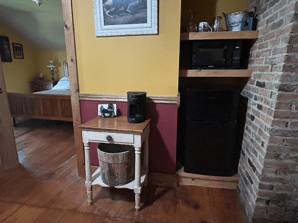 small table with a small black coffee pot on it with a mini fridge and a microwave to the right