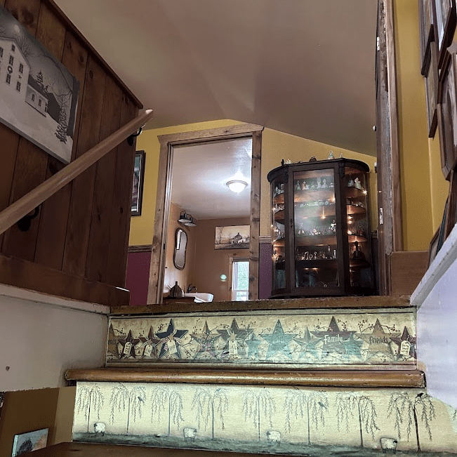 View going up the stairs looking into a bathroom with a curio cabinet lit up next to the door