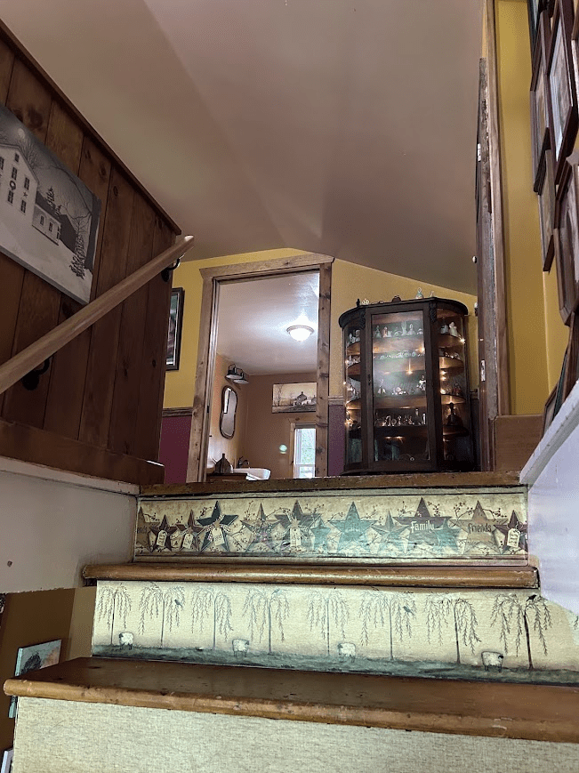 View going up the stairs looking into a bathroom with a curio cabinet lit up next to the door