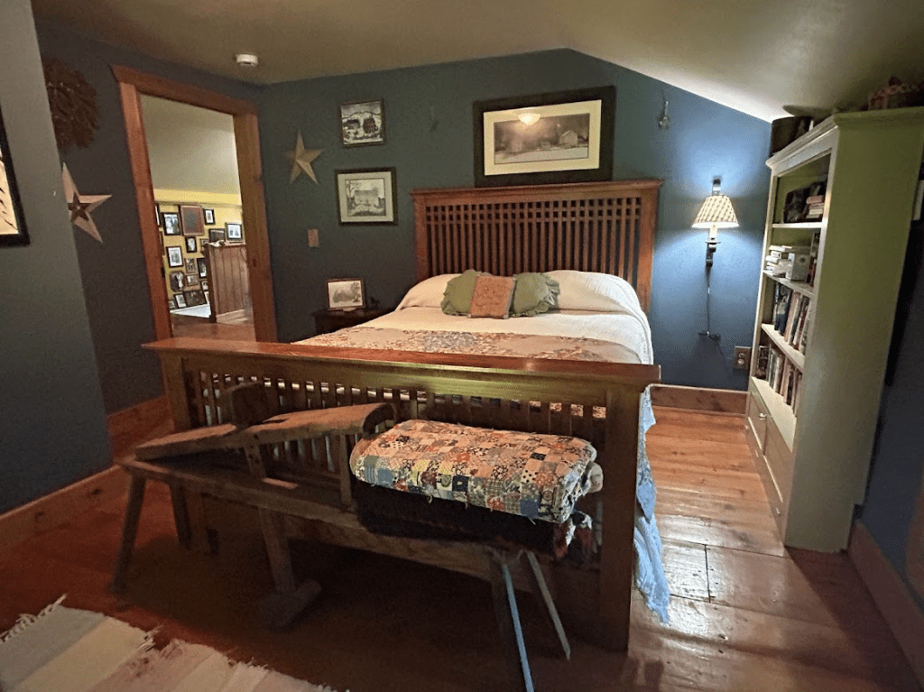 queen bed in a room with blue walls with a white bookcase and a bench at the foot of the bed