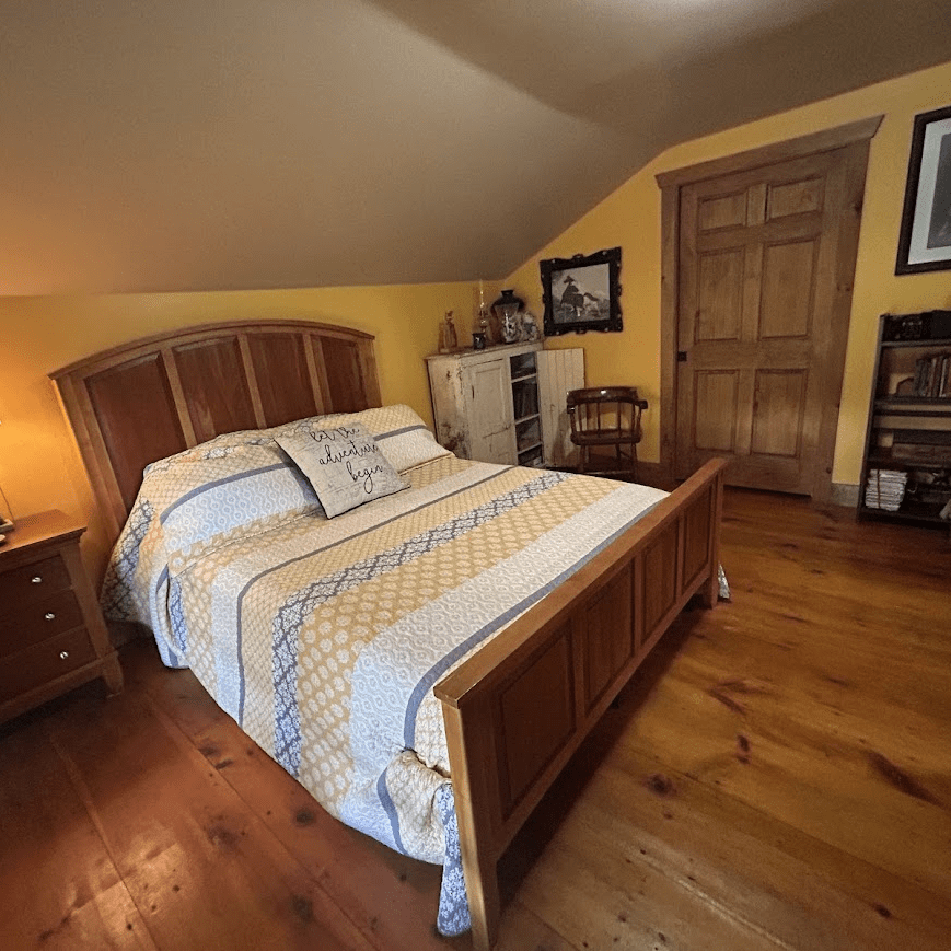 queen bed in a room with yellow walls taken towards the bedroom door